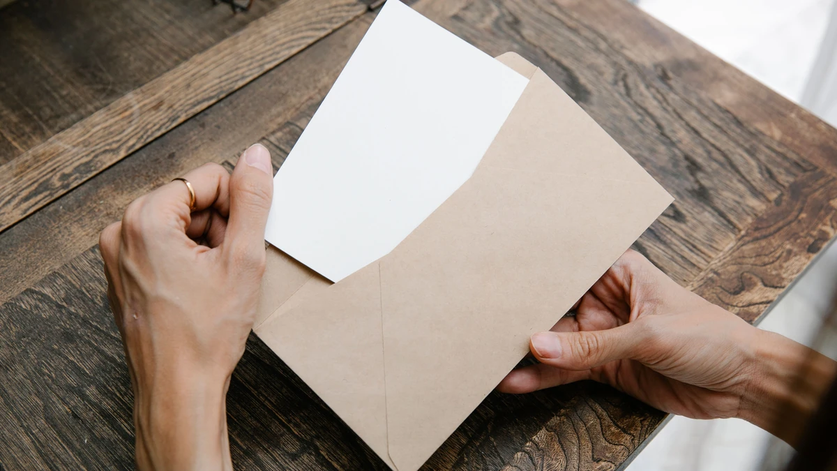 Hands opening a paper envelope containing a letter on a wooden table