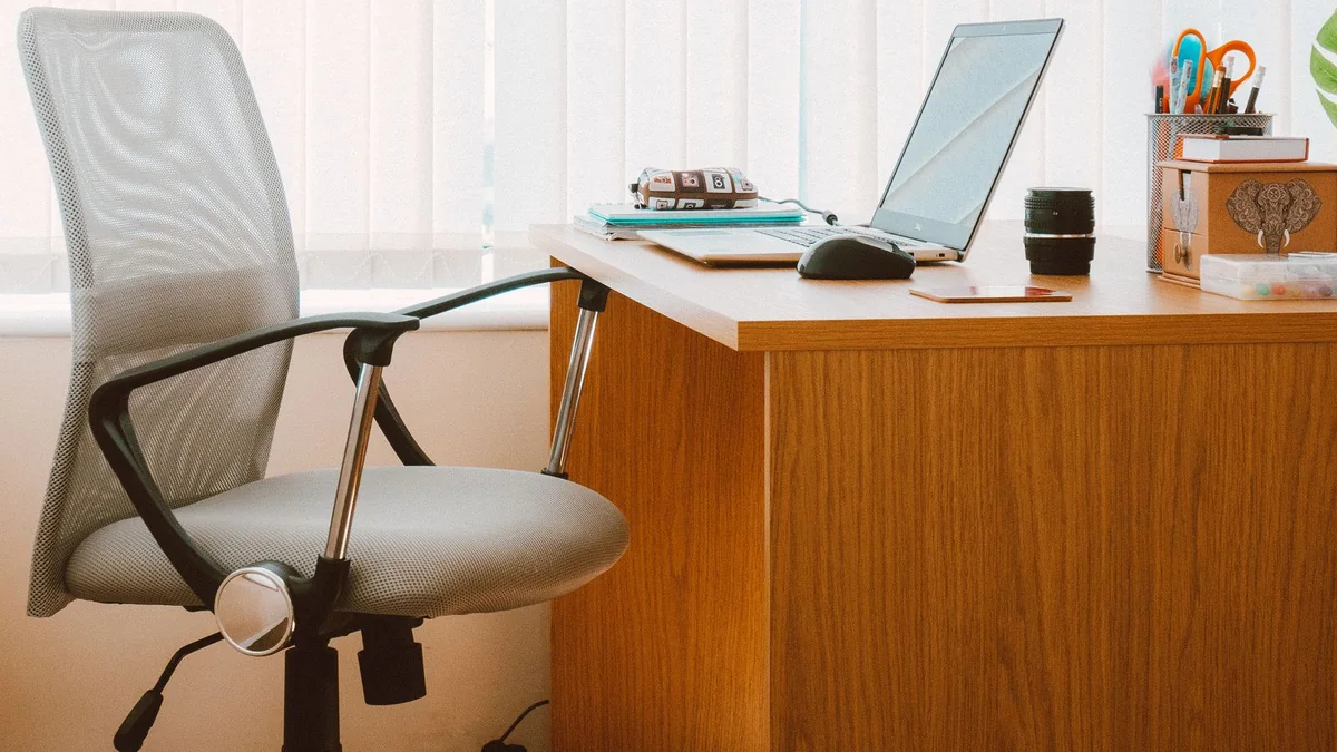An empty office chair beside a desk with a laptop in bright window light