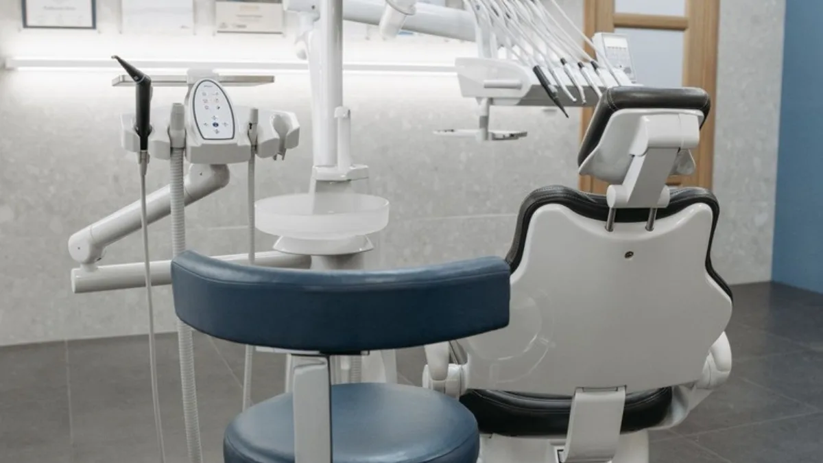 An empty dental treatment chair and instrument tray in a bright clinic room