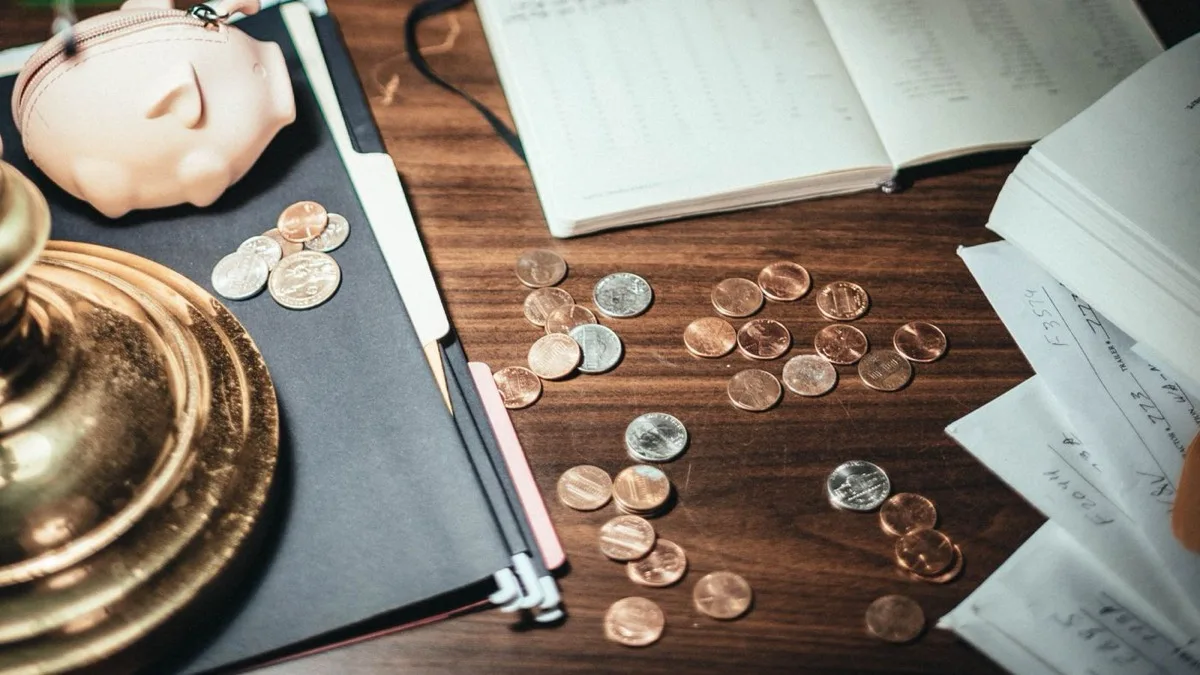 A piggy bank, scattered coins, a ledger and receipts on a dark wooden desk