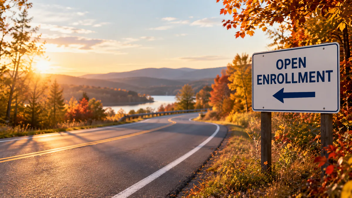 A roadside sign reading Open Enrollment with an arrow pointing left, beside a two-lane road running through autumn trees at sunset