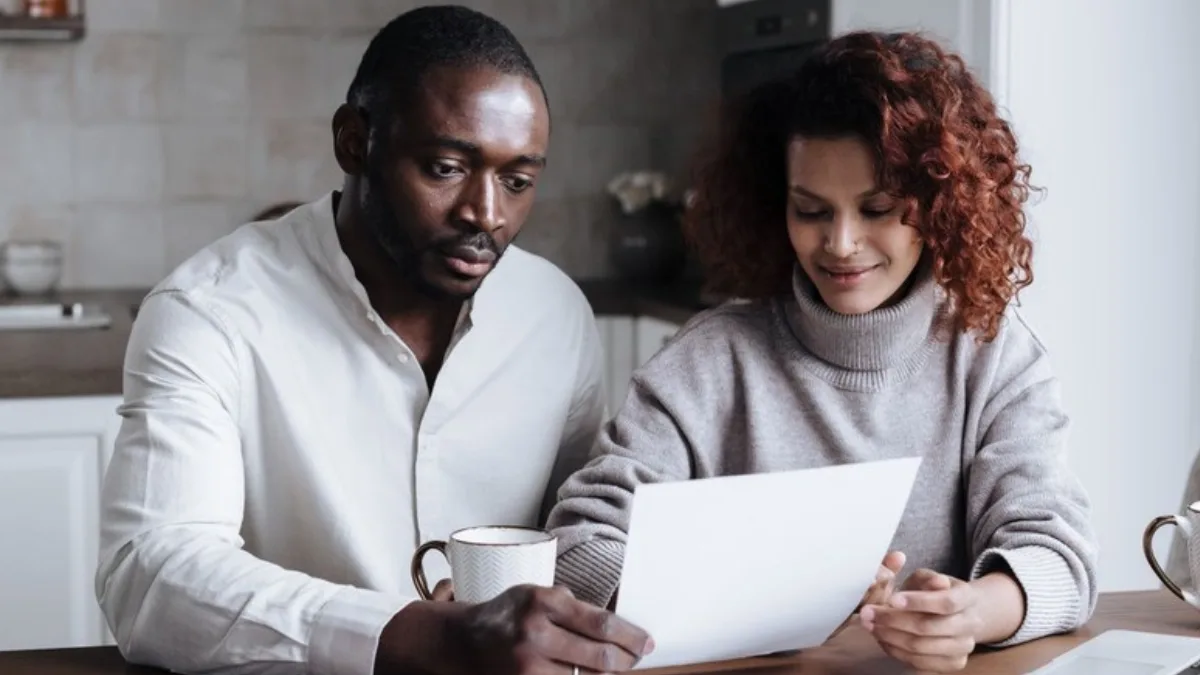 Two people at a kitchen table reading a letter together over coffee
