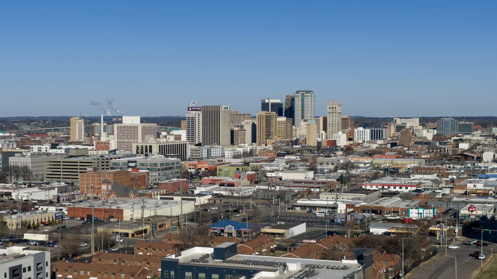 The downtown Birmingham skyline seen from above, office towers rising behind the low brick rooftops of the surrounding blocks