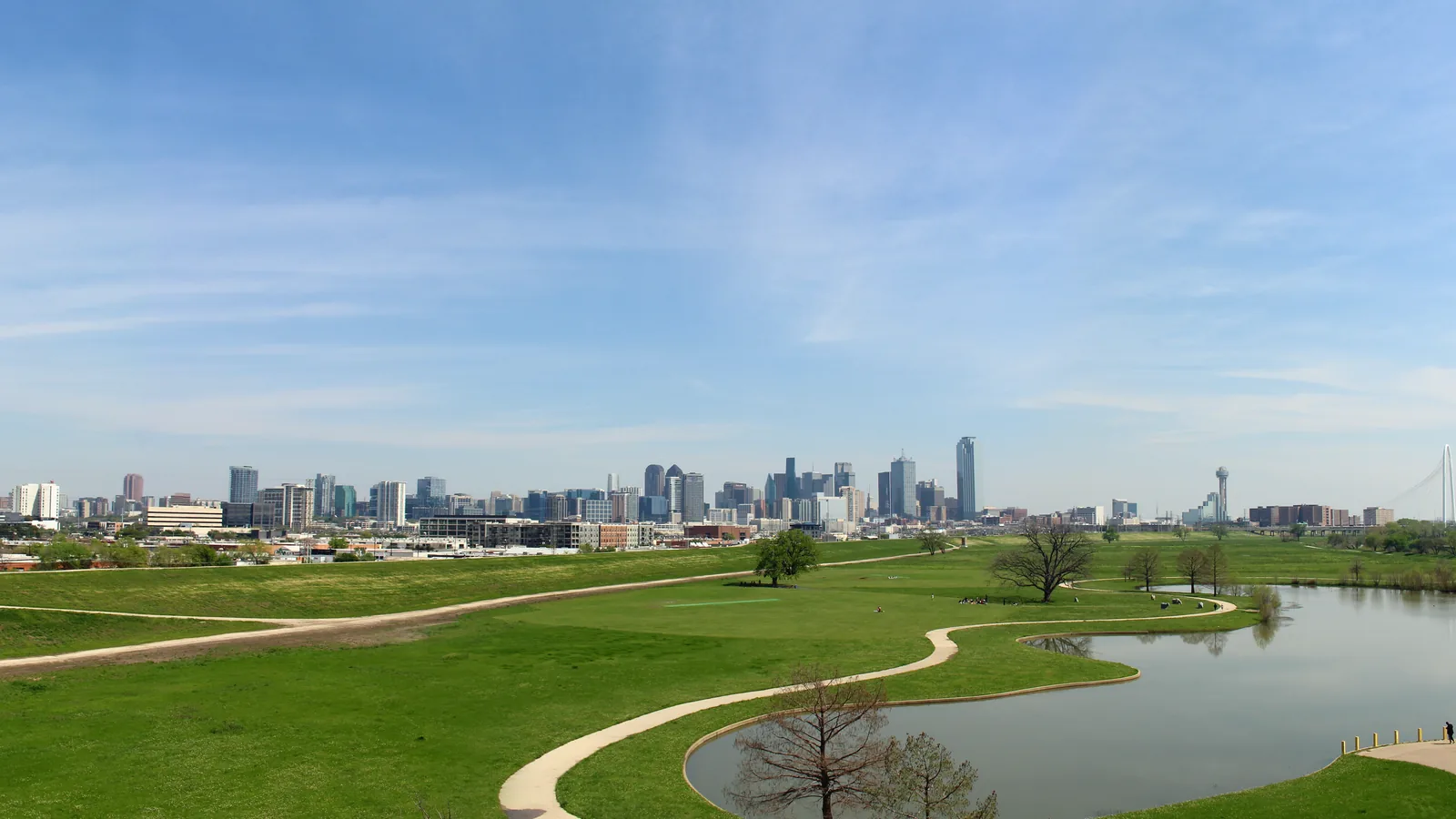 The Dallas skyline seen across the open meadows and still water of Trammell Crow Park on the Trinity River