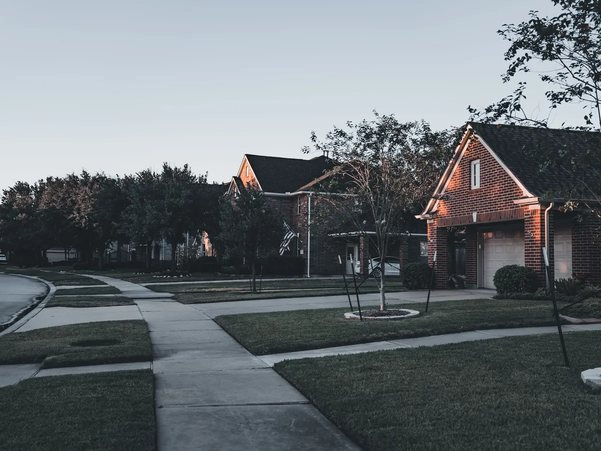A quiet residential street of brick homes at dusk with warm porch light
