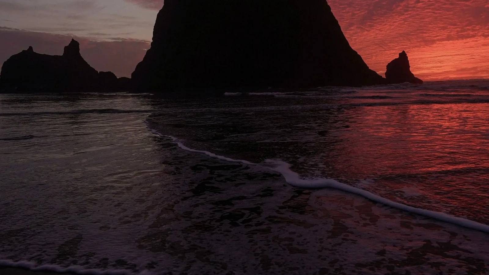 Haystack Rock and the sea stacks at Cannon Beach on the Oregon coast, silhouetted against a red sunset